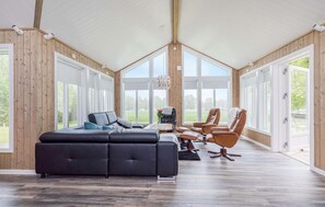 A spacious room with a large black sectional sofa, a dining table with chairs, and large windows offering a view of the outdoors.