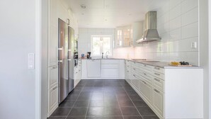 A modern kitchen with white cabinetry, a stainless steel refrigerator, a built-in oven, and a large window providing natural light.