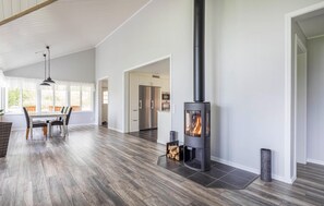Cozy living area with a high ceiling, large window, and wood-burning stove, perfect for relaxing.