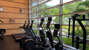 Une salle de sport équipée de tapis de course, de vélos elliptiques et d’appareils de musculation, avec de grandes fenêtres donnant sur un espace verdoyant.