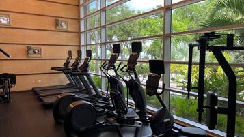 Une salle de sport équipée de tapis de course, de vélos elliptiques et d’appareils de musculation, avec de grandes fenêtres donnant sur un espace verdoyant.