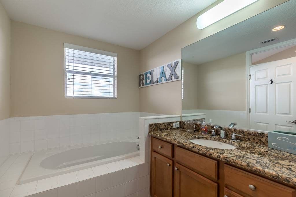 Un baño con bañera, dos lavamanos, tocador con cajones, un espejo grande y un cartel con la palabra 'RELAX'.