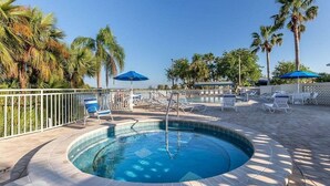Une piscine circulaire entourée d’une terrasse, de chaises longues et de parasols.