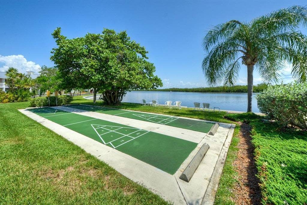 Una cancha de shuffleboard con vista al lago, rodeada de follaje y palmeras.
