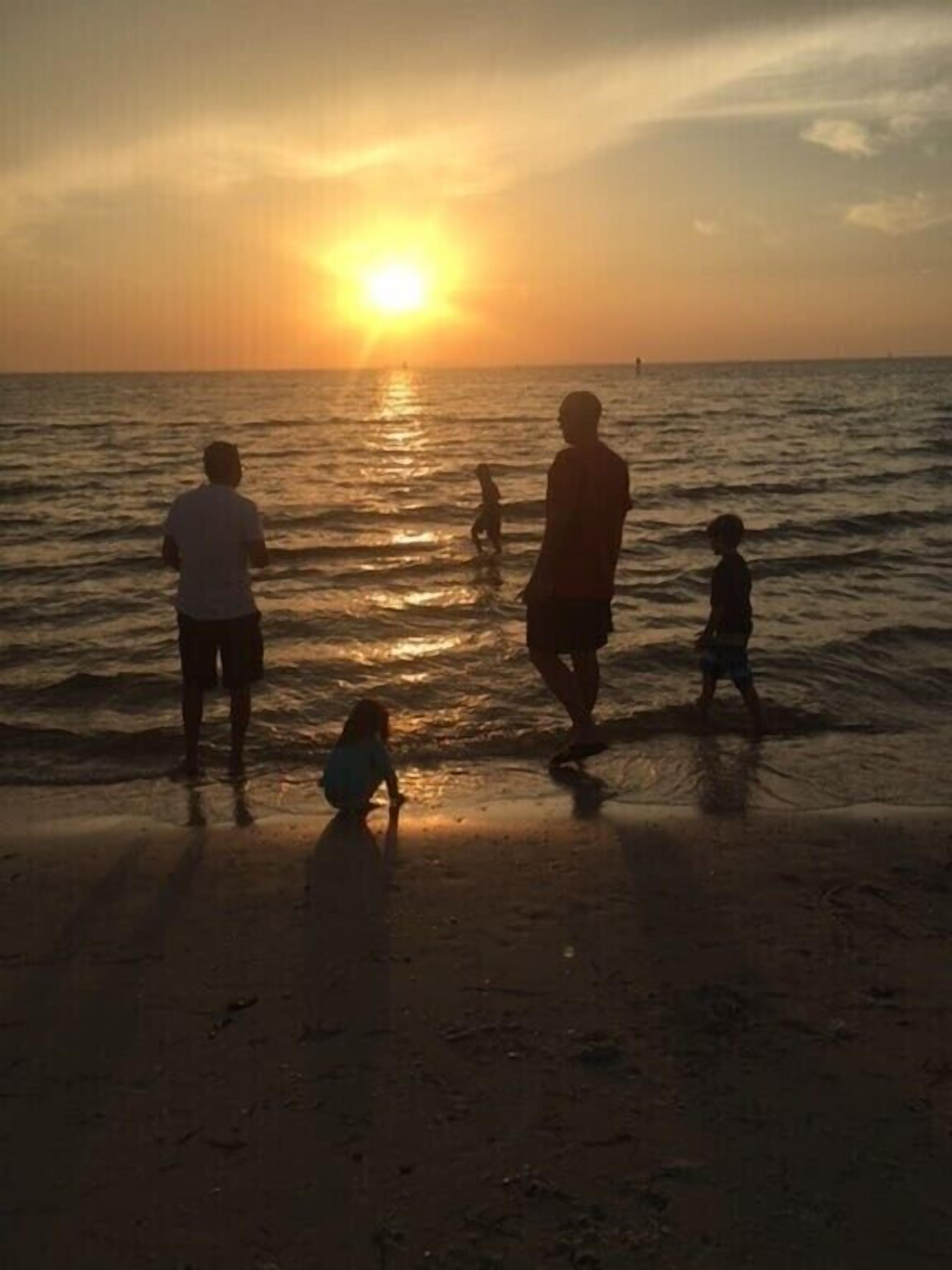 Un atardecer en la playa con gente de pie y caminando por la orilla.