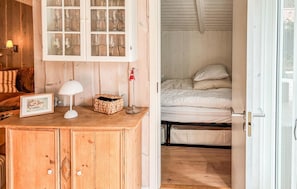 Una habitación de madera con una cama, un aparador con puertas de cristal, una lámpara y un cuadro enmarcado.