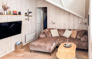 Una sala de estar acogedora con un sofá modular, un televisor de pantalla plana y una pared de madera.