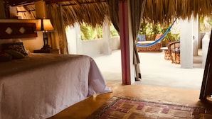 A room with a bed, a nightstand, a lamp, a hammock, and a view of the outdoors. - Hacienda la Rusa (Barra de Potosi)