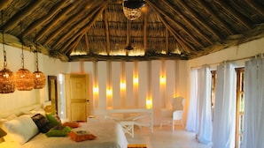 A spacious bedroom with a large bed, a wooden ceiling, hanging lights, a small table, and a chair. - Hacienda la Rusa (Barra de Potosi)