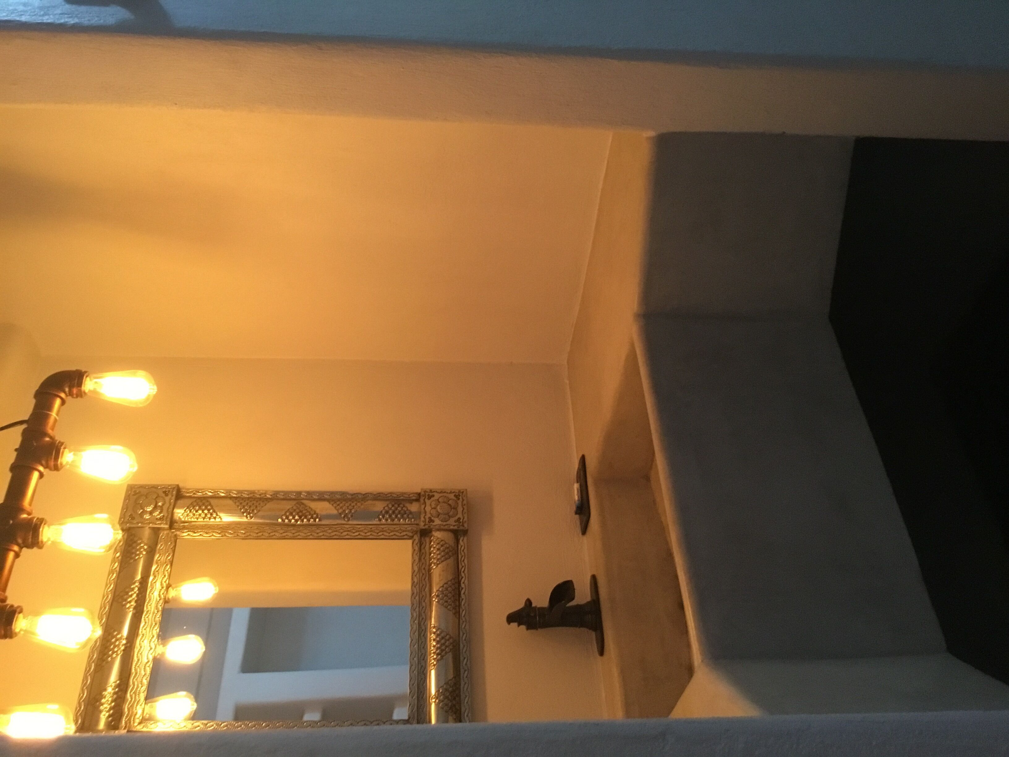 Een spiegel met verlichting rond de rand, een lichtschakelaar op de muur, en een hoek van een kamer met een wit plafond.