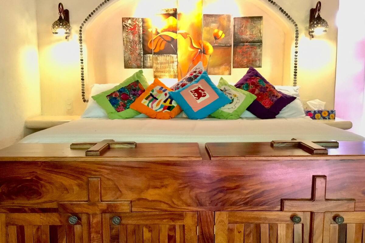 A bed with colorful pillows, a wooden headboard, and wall-mounted lights.
