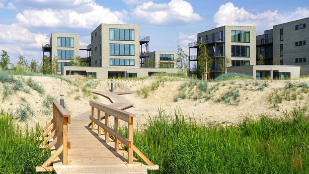 A wooden boardwalk leading to modern buildings with balconies and large windows. - Cozy apartment in Lembruch/Dümmer See with indoor swimming pool (Lembruch/Dümmer See)