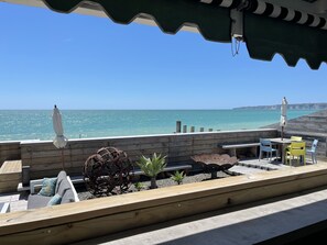 A wooden deck with seating, a table, and chairs overlooking a beach. - The Cape View Pacific Ocean  Experience (Haumoana)