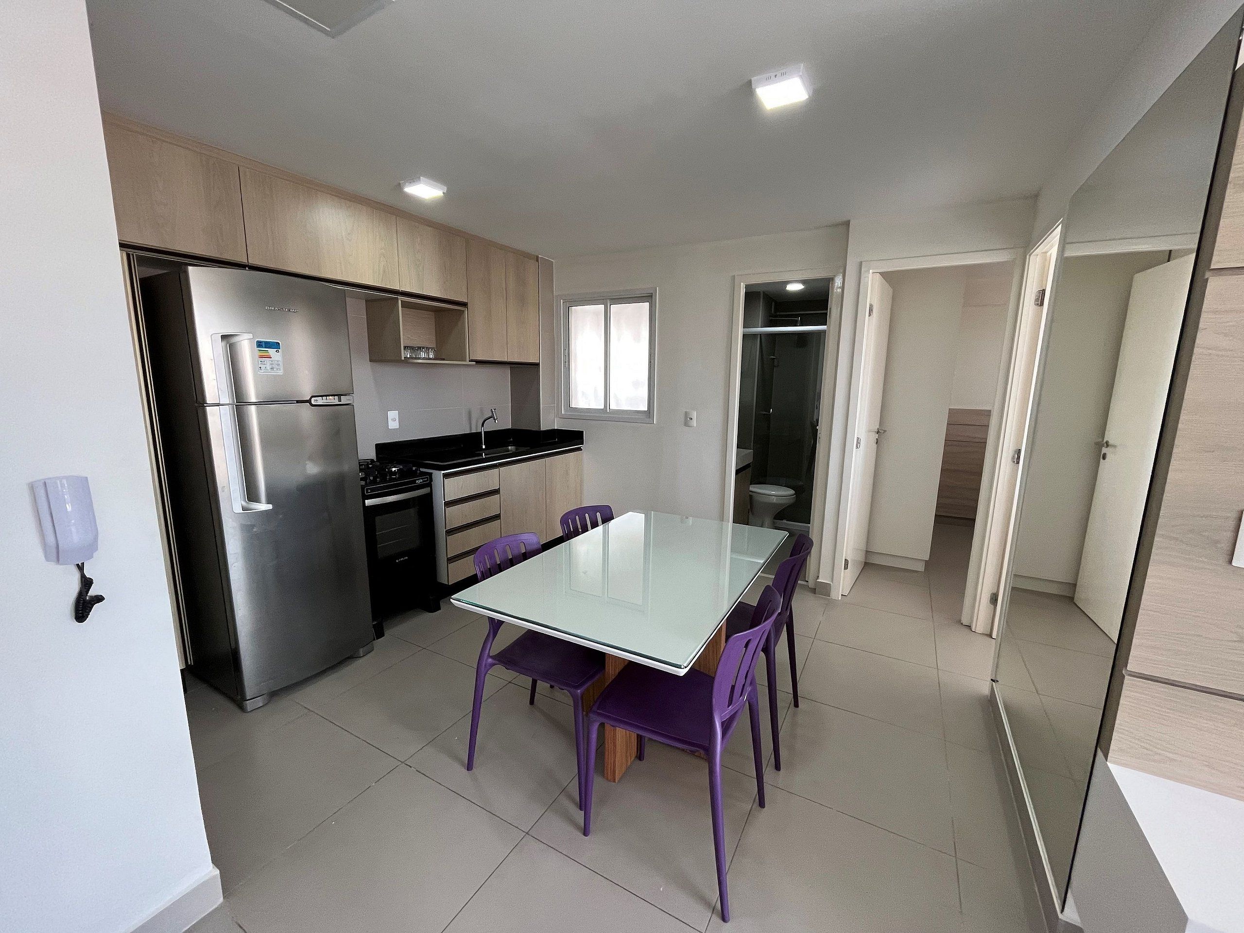 Una cocina compacta con electrodomésticos modernos, una mesa de comedor con sillas y un baño a la vista.