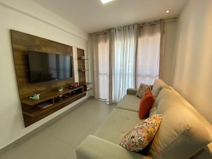 A living room with a flat-screen TV, wooden entertainment unit, sofa, and curtains. - Compacto de Luxo - Helbor My Way (Fortaleza)