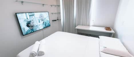 A hotel room with a bed, a TV mounted on the wall, a small table, and a window with curtains.
