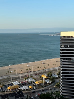 A coastal view with a beach, palm trees, and a modern building with balconies. - Compacto de Luxo - Helbor My Way (Fortaleza)