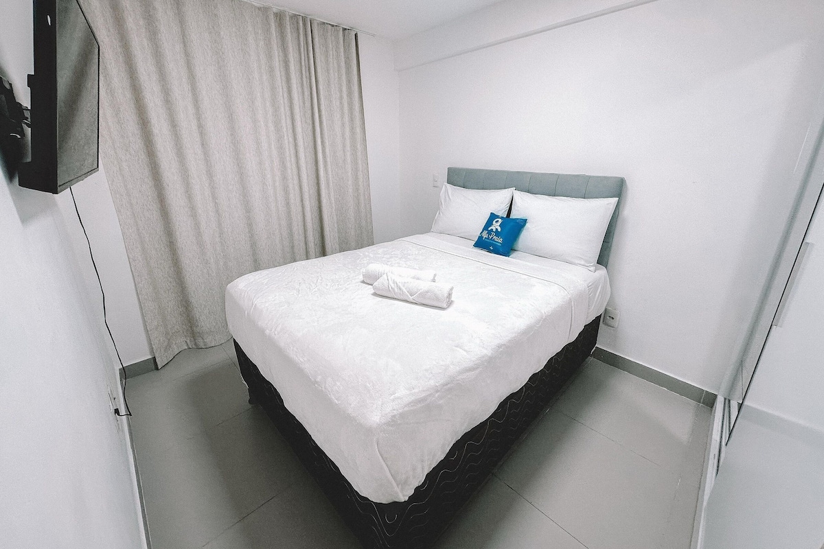 A hotel room with a bed, a TV mounted on the wall, and a curtain.