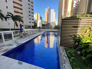 A swimming pool with a view of tall buildings in the background. - Compacto de Luxo - Helbor My Way (Fortaleza)