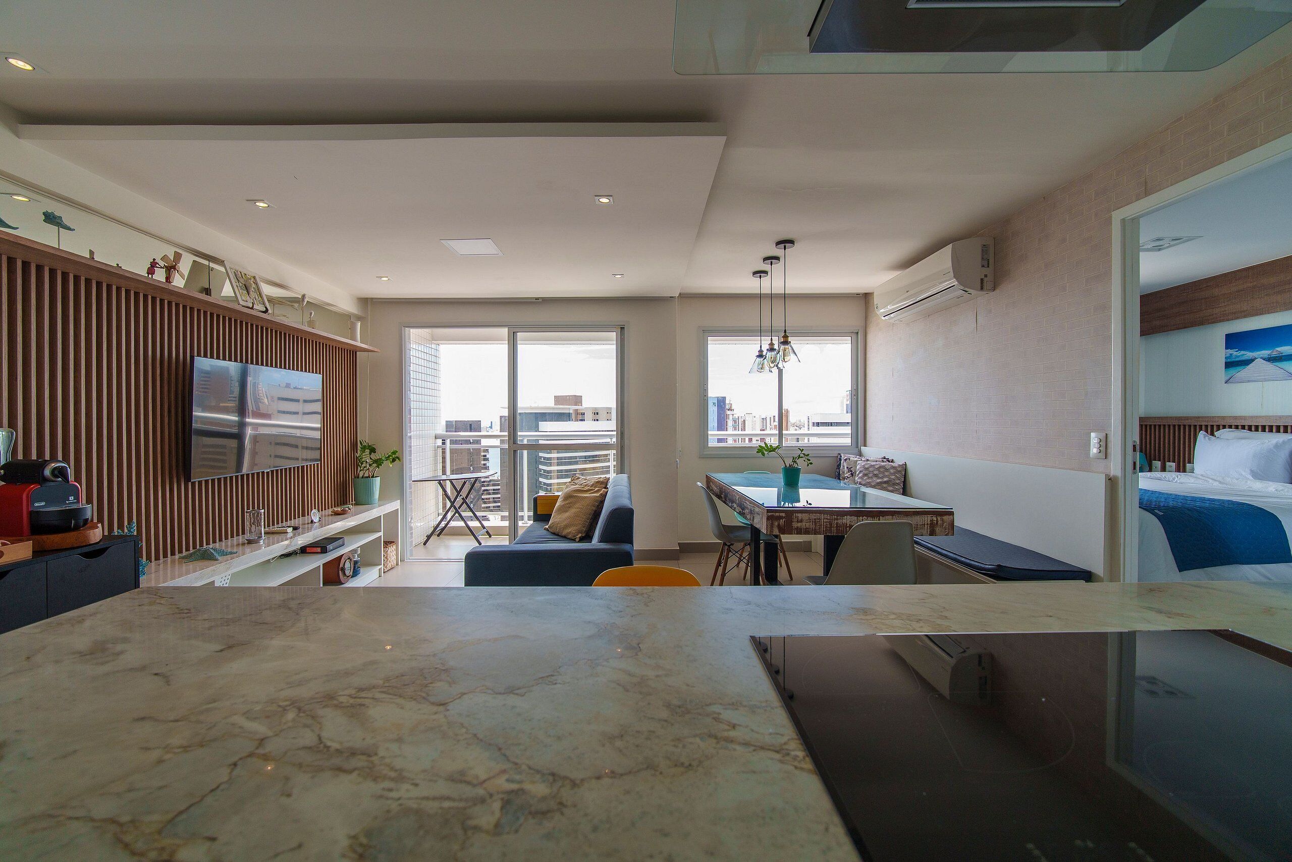 Une chambre d’hôtel moderne dotée d’une grande fenêtre, d’un coin repas, d’un espace de vie avec un canapé et d’un coin cuisine avec un plan de travail en marbre.