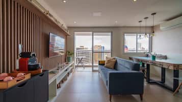 Una sala de estar moderna con sofá, mesa de comedor, televisor y área de cocina con electrodomésticos.