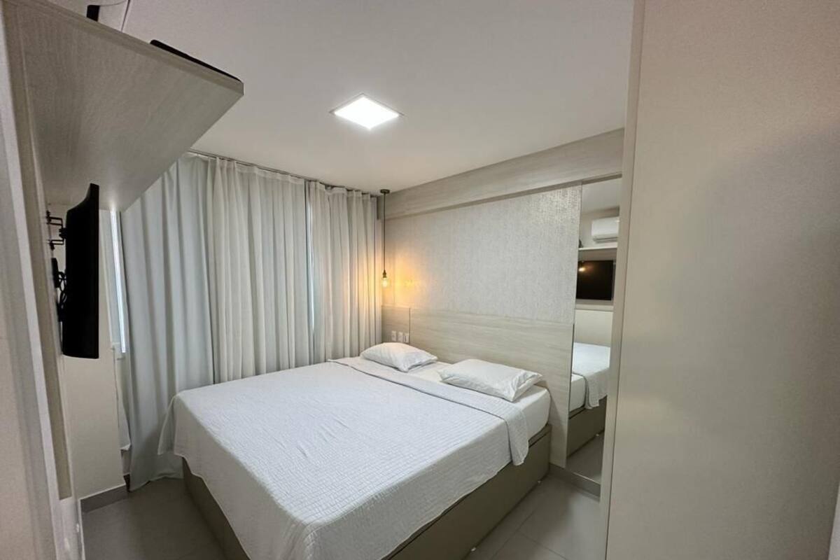 A hotel room with a bed, curtains, a wall-mounted TV, and a ceiling light.