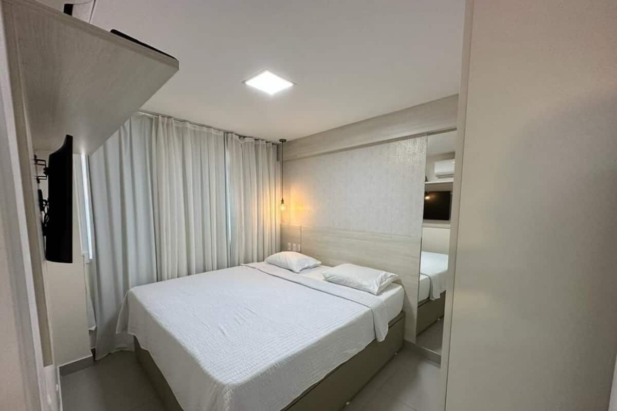 A hotel room with a bed, curtains, a wall-mounted TV, and a ceiling light.