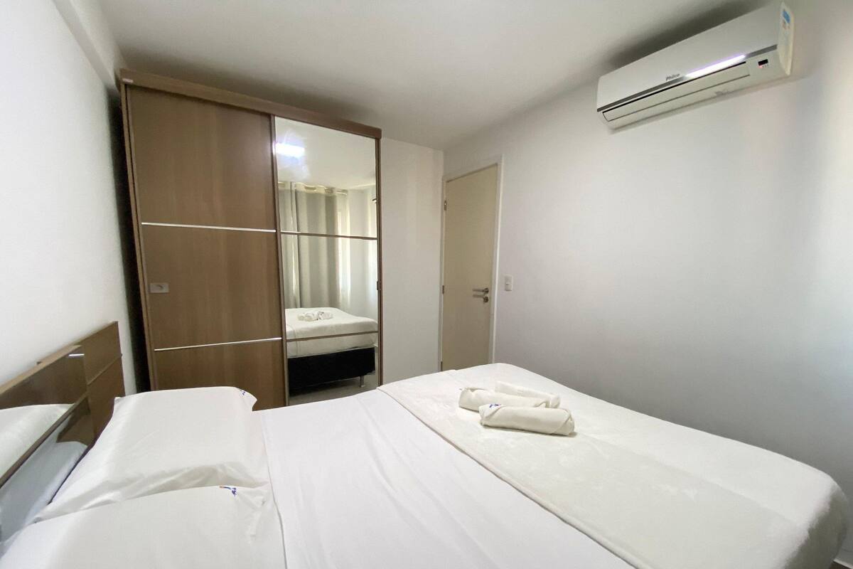 A hotel room with a bed, a wardrobe, a mirror, and an air conditioning unit.