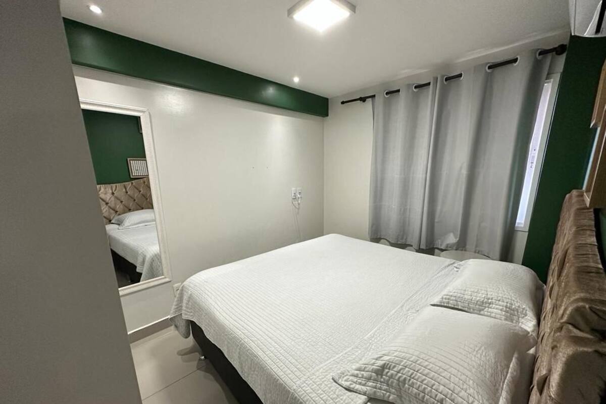 A bedroom with a bed, a mirror, a window with curtains, and a green accent wall.
