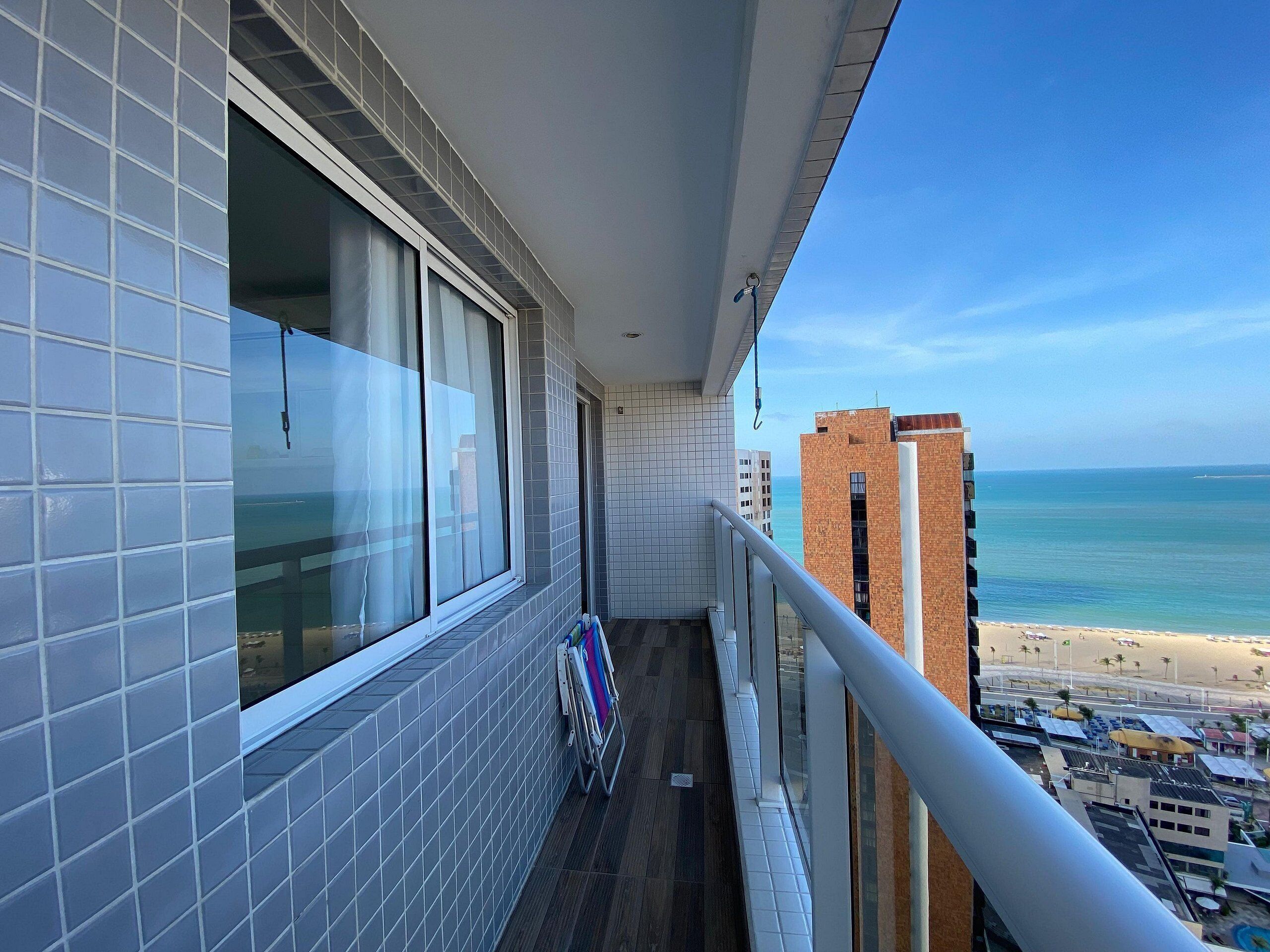 Un balcon avec vue sur la plage et l’océan, des murs carrelés et une rambarde en métal.