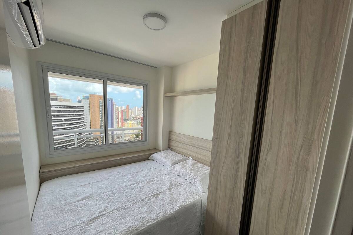 A hotel room with a bed, a window with a city view, and a wooden headboard.