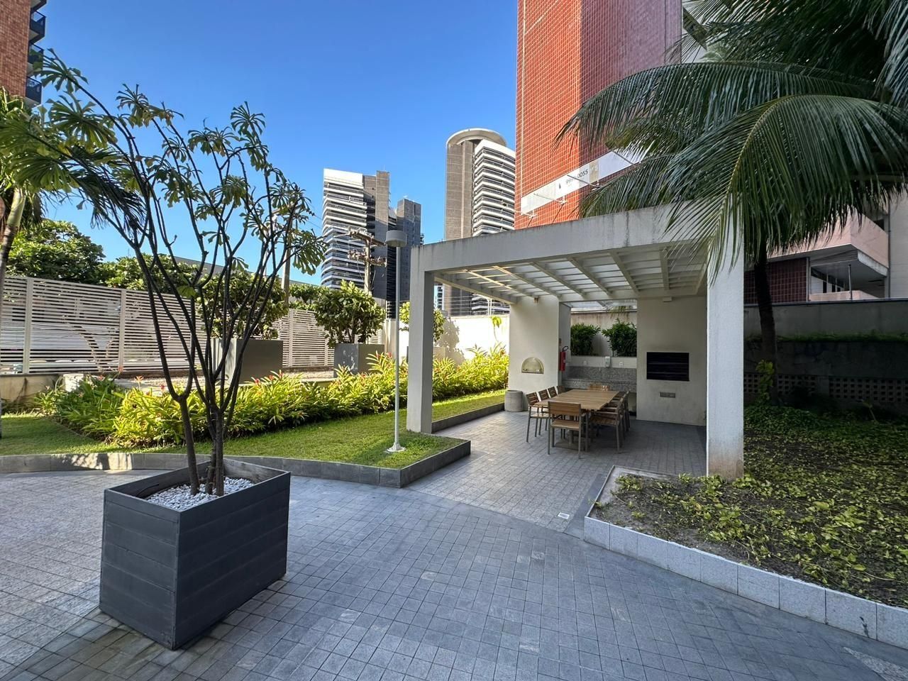 A courtyard with a covered seating area, a planter with a tree, and a paved walkway.