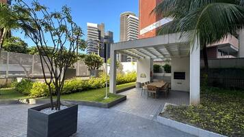 A courtyard with a covered seating area, a planter with a tree, and a paved walkway.