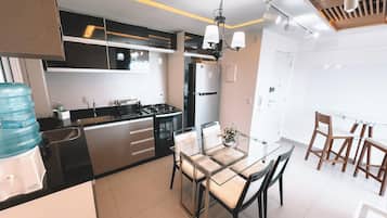 Une cuisine moderne équipée d’une cuisinière à gaz, d’un réfrigérateur et d’un coin repas avec une table en verre et des chaises en bois.