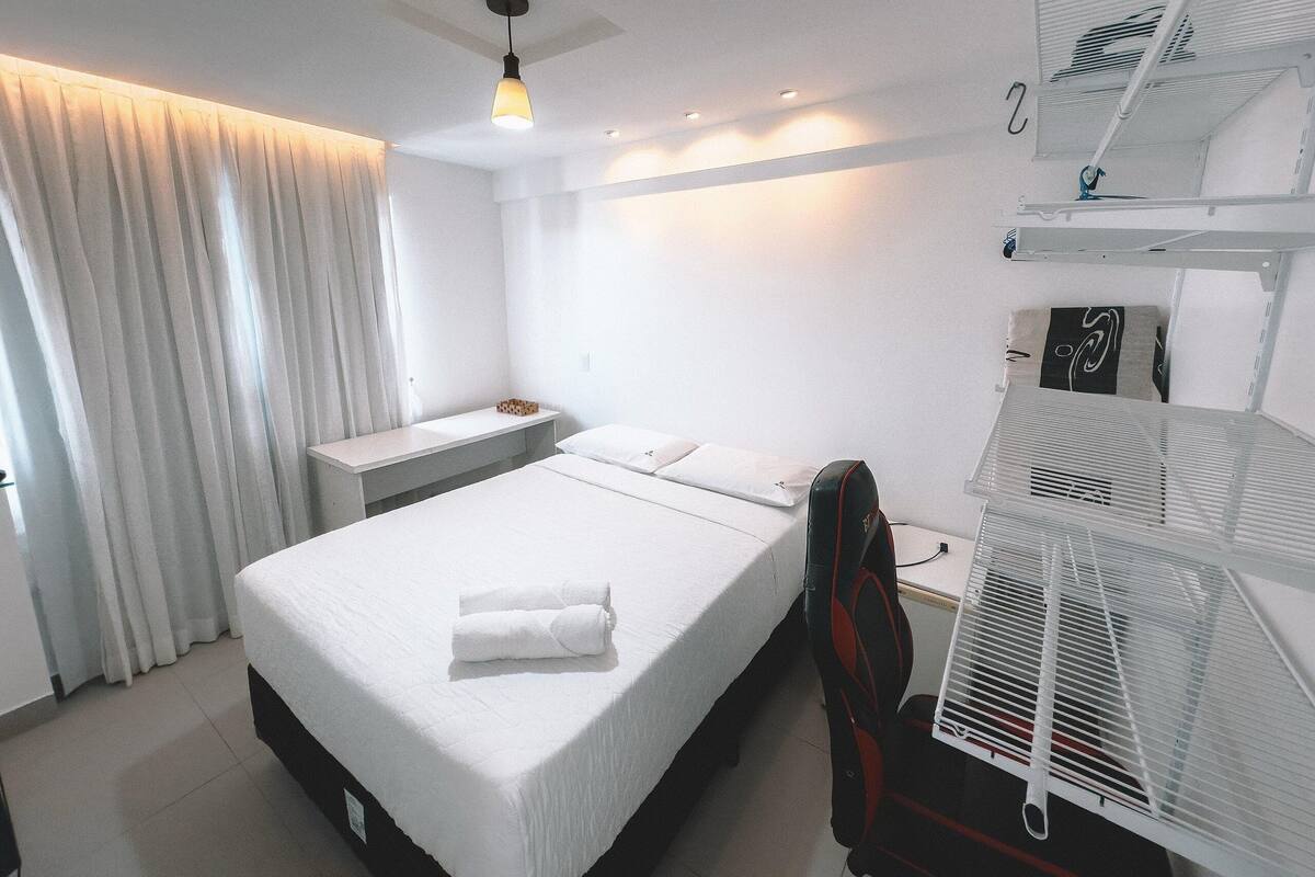 A hotel room with a bed, a desk, a chair, a ceiling fan, and a window with curtains.