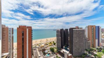 A high-rise building with a curved facade, a beach in the background, and a clear sky.