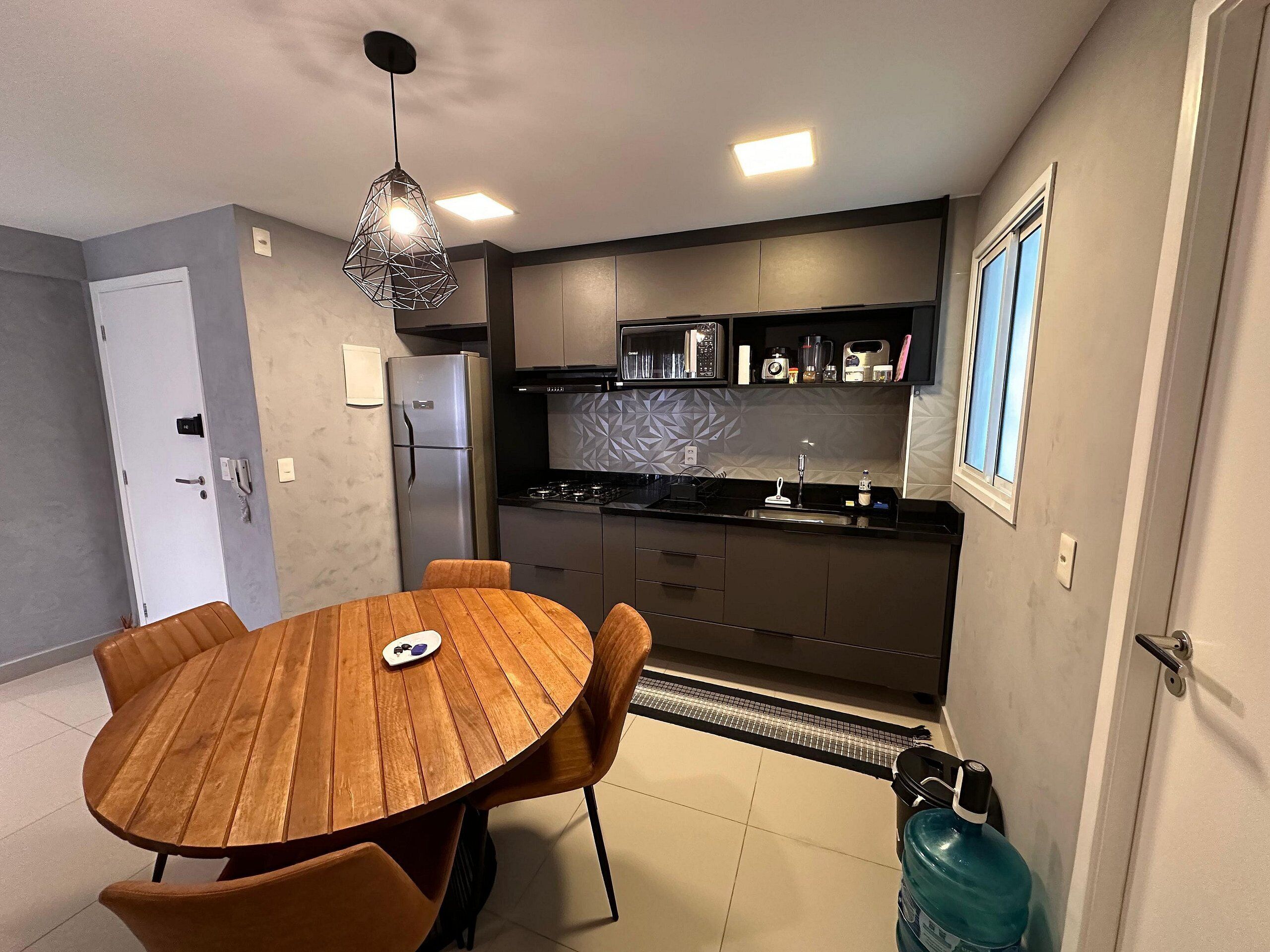 Una cocina moderna con comedor, que incluye una mesa redonda de madera y sillas, horno empotrado y refrigerador.