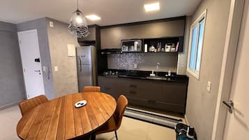 Una cocina moderna con comedor, que incluye una mesa redonda de madera y sillas, horno empotrado y refrigerador.