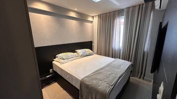 Un dormitorio moderno con cama, cortinas, una lámpara de techo y un televisor montado en la pared.