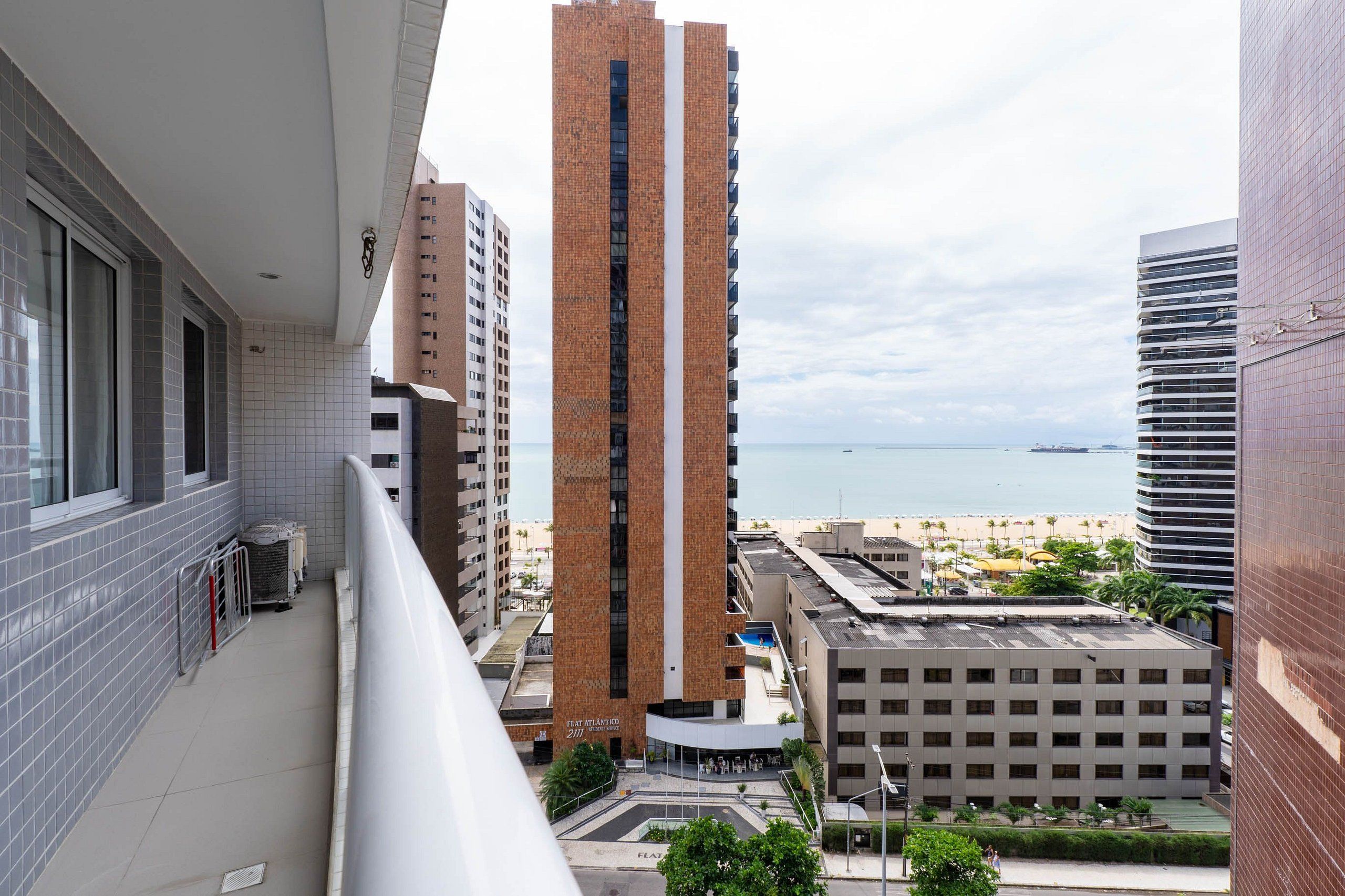 Un edificio alto con un hueco central para ascensores, rodeado de otros edificios y una playa al fondo.
