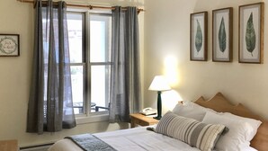 Un lit bien fait, avec une couverture grise, une lampe de chevet et un tableau encadré accroché au mur.