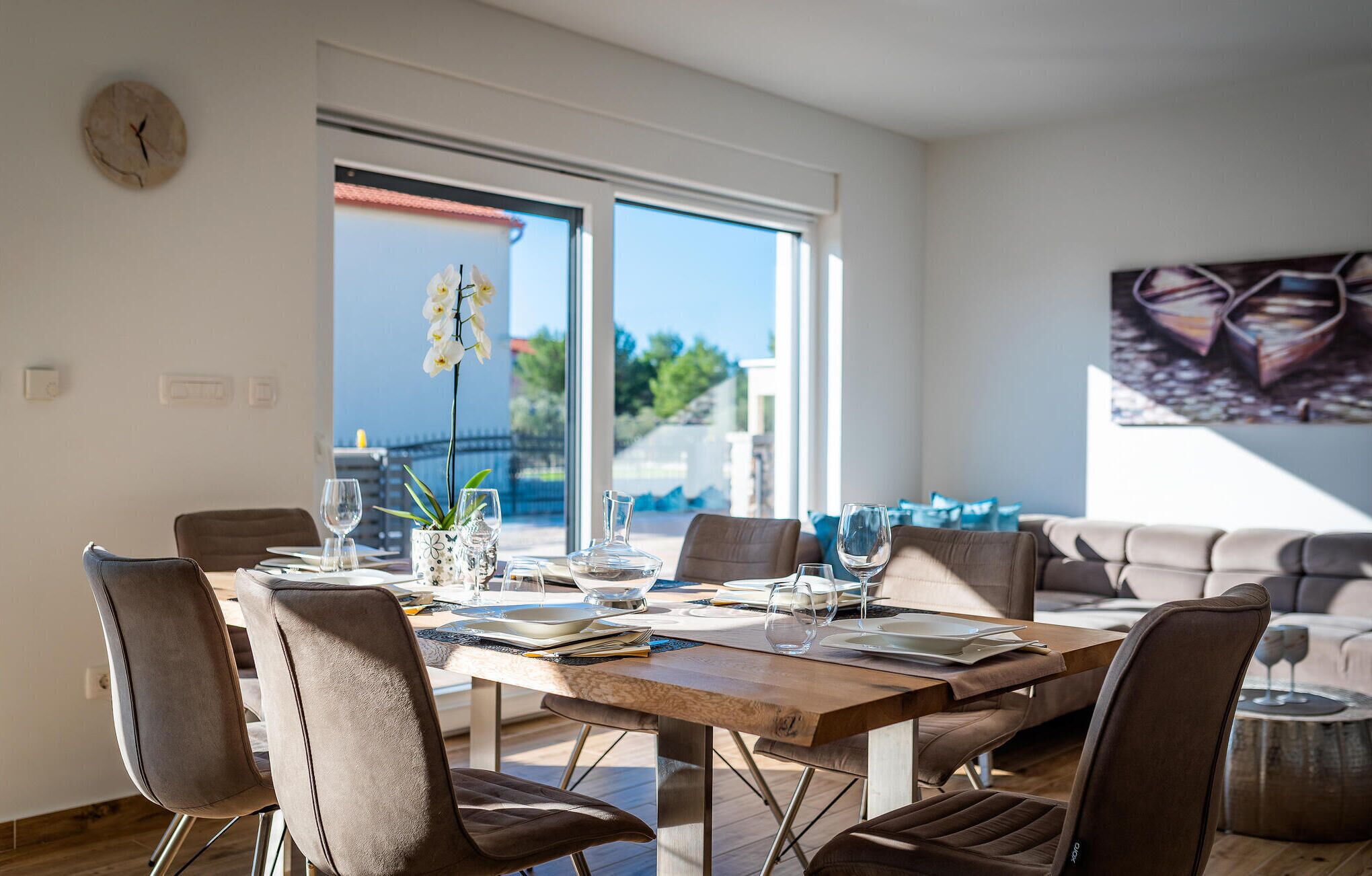 A modern dining area with a wooden table, multiple chairs, and a view of the outdoors through large windows.