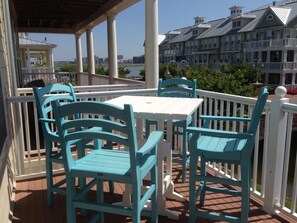 Un espace extérieur abrité, aménagé avec une table blanche et des chaises turquoise, offrant une vue sur le bord de l’eau et les bâtiments qui se dressent à l’arrière-plan.