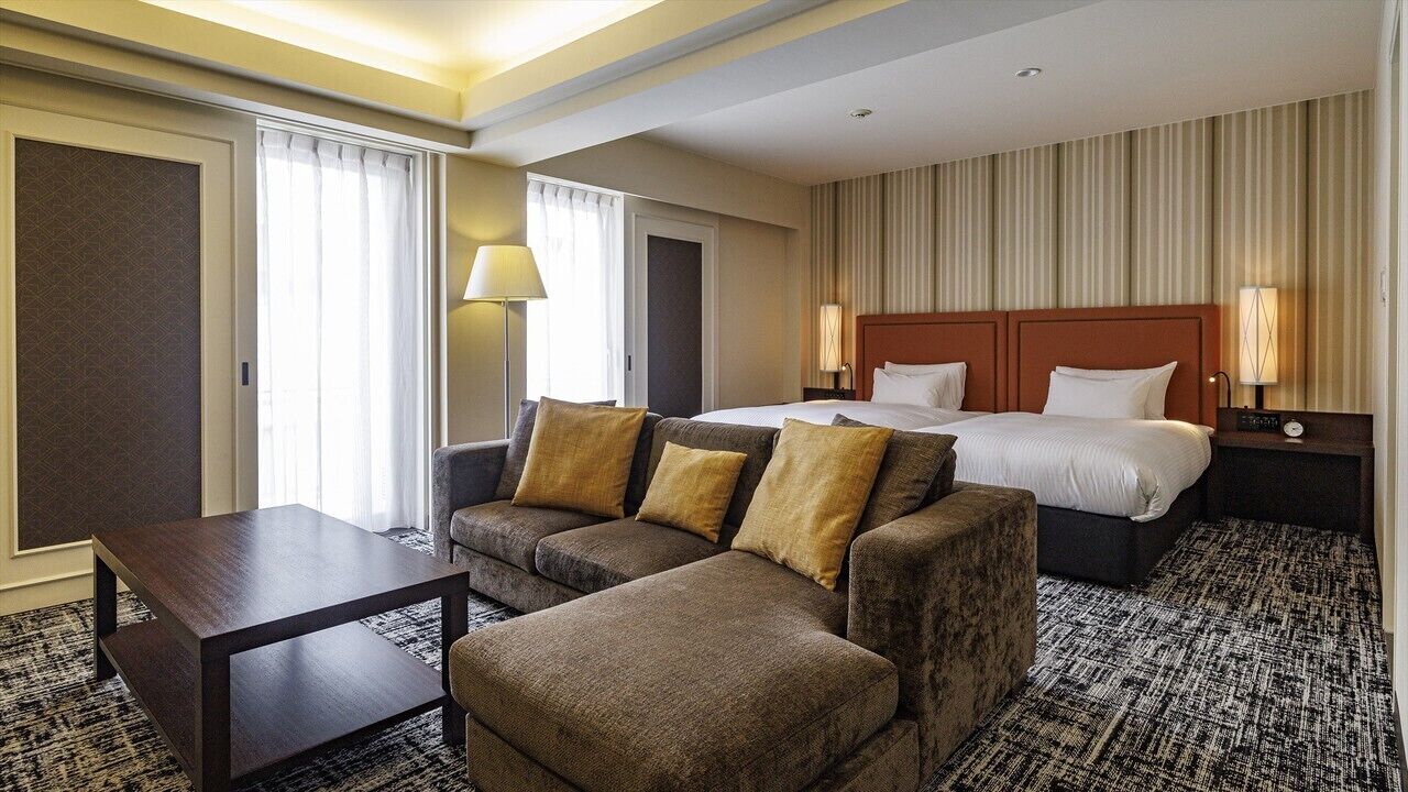 A hotel room with a bed, two sofas, a small table, and a nightstand with lamps.