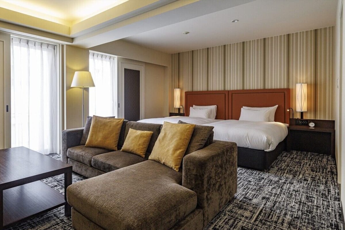 A hotel room with a bed, two sofas, a small table, and a nightstand with lamps.