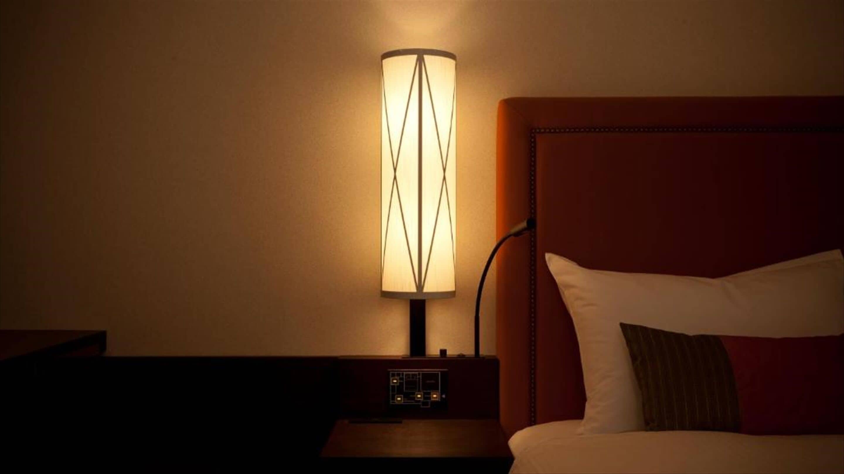 A hotel room with a bed, a nightstand, and a lamp.