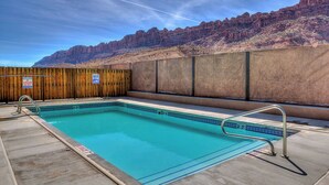 A swimming pool with a wooden fence and a lifeguard sign, surrounded by a mountainous landscape. - Canyon & Sky: Hot Tub Sanctuary, Redrock Patio Lounge, & Sunset Deck Views! SG2 (Moab)
