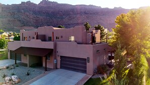 A modern two-story building with a flat roof, a garage, and a landscaped front yard with rocks and plants. - Canyon & Sky: Hot Tub Sanctuary, Redrock Patio Lounge, & Sunset Deck Views! SG2 (Moab)