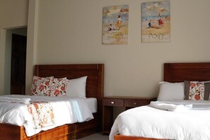 Two single beds with white linens and floral-patterned pillows, a nightstand, and a wall-mounted side table.