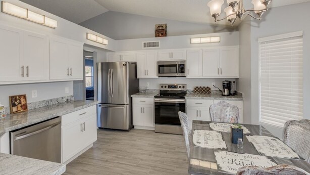 A modern kitchen with white cabinets, stainless steel appliances, and a dining area with a table set for four. - Beautiful remodeled home to enjoy your stay. (Phoenix)
